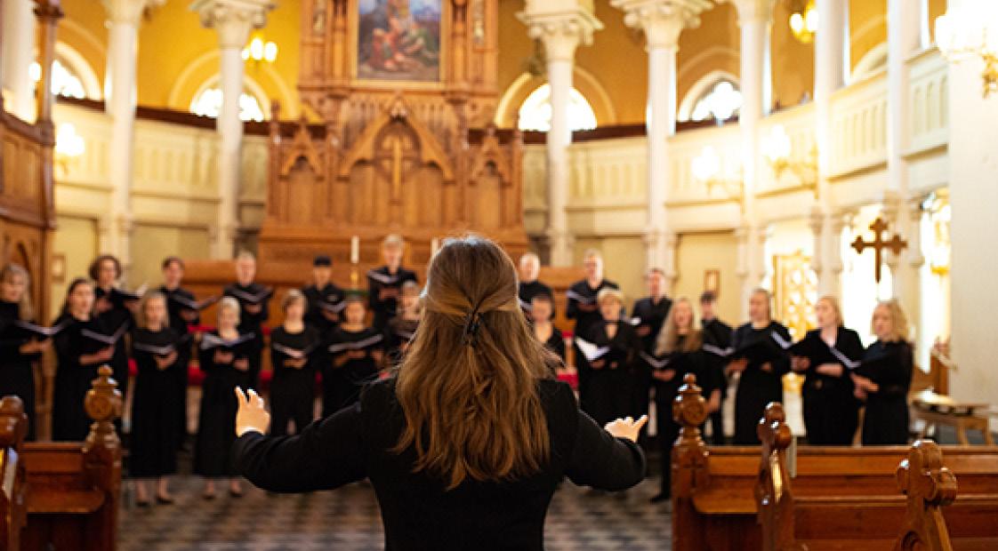 Finlands ungdomskör uppträder i en kyrka. Framför kören står en dirigent.